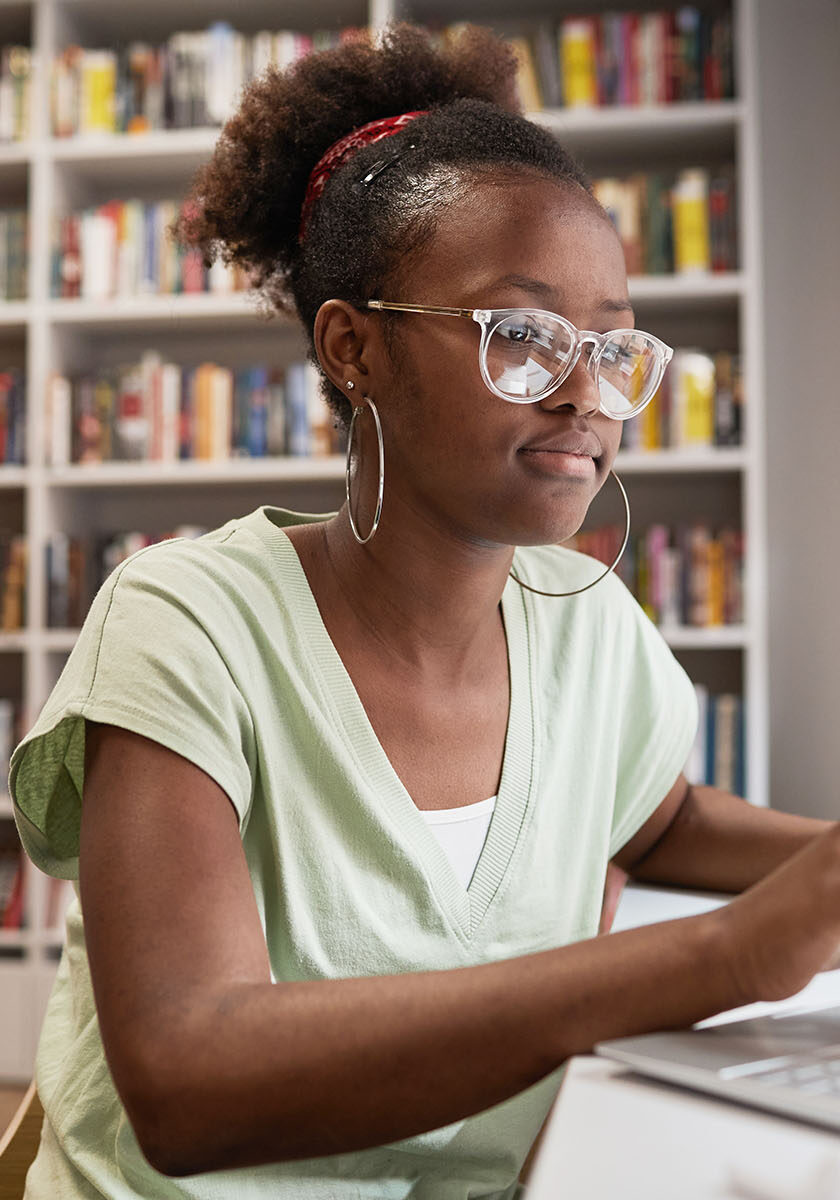 Side view portrait of young African-American woman typing at laptop keyboard while studying in school library, copy space