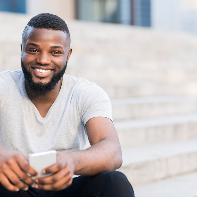 Portrait of casual african guy sitting on stairs and smiling outdoor, copy space
